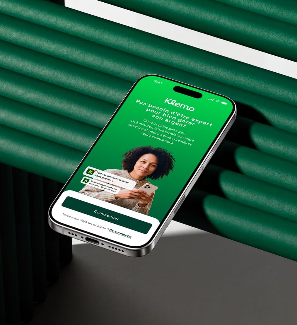 L'écran d'accueil de l'application Klemo sur un iPhone posé de biais devant des reliefs verts : une invitation à faire le point sur sa situation, une femme son téléphone en main, et le bouton « Commencer »