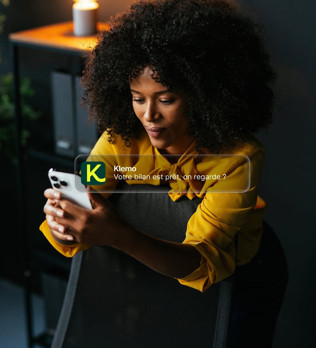 Une femme assise sur une chaise, son téléphone en main, et une notification de Klemo : « Votre bilan est prêt, on regarde ? »