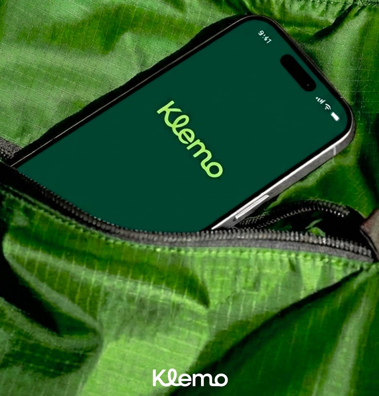 Un iPhone affichant le logo Klemo, glissé dans la poche zippée d'une veste verte