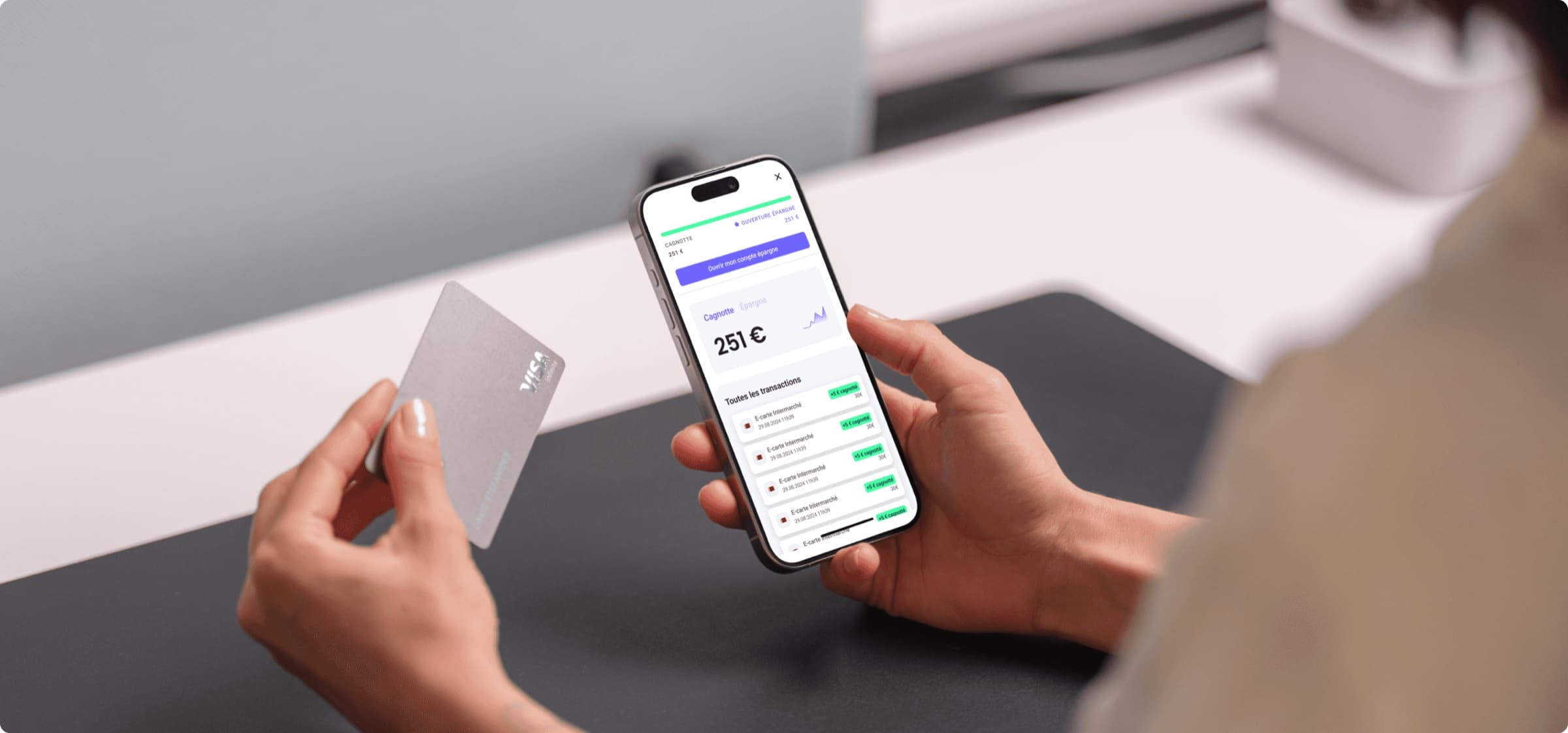Au comptoir d'un commerce, quelqu'un tient son téléphone sur l'écran cagnotte de Salva, 251 €, et une carte bancaire dans l'autre main